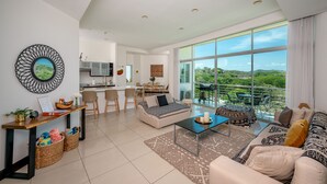 A spacious living area with a large window, a sofa, a coffee table, and a dining area with chairs and a table. - PERFECT LUXURY stay steps to the ocean, amazing food, and lots of live music!  (Tamarindo)