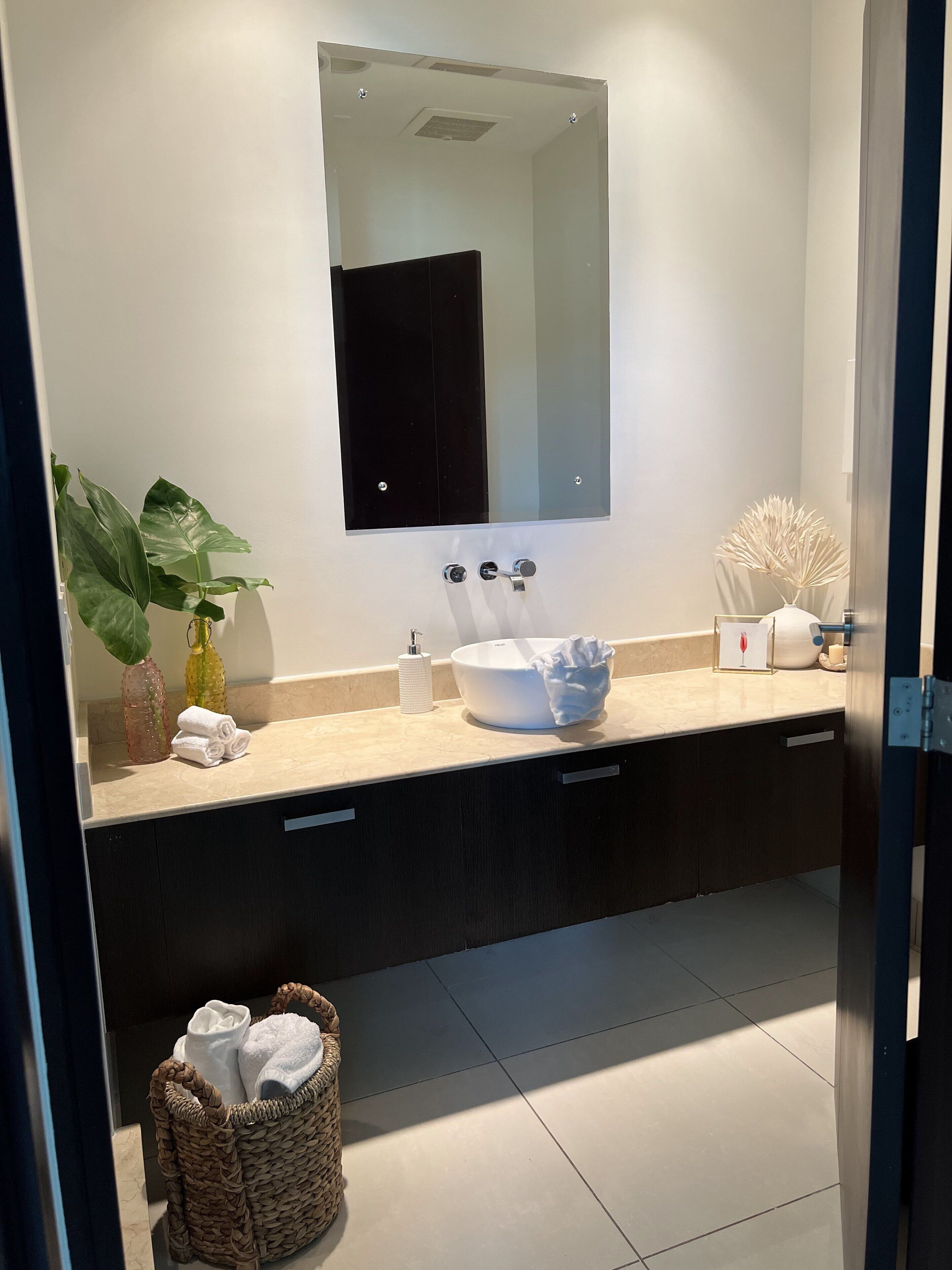 Een moderne badkamer met een witte wastafel, donkere kastjes en een grote spiegel.
