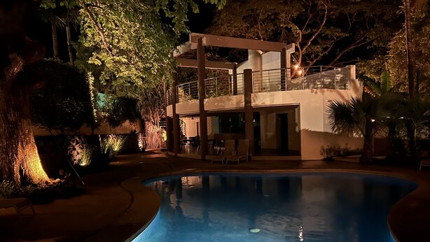 A modern pool area with a clear pool, surrounded by lush greenery and a multi-level building with outdoor seating. - PERFECT LUXURY stay steps to the ocean, amazing food, and lots of live music!  (Tamarindo)