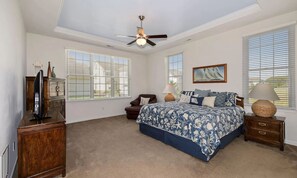A bedroom with a bed, a ceiling fan, a dresser, a chair, and a lamp.