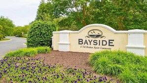 Schild für Bayside, eine Ferienanlage von Toll Brothers, mit einem begrünten Eingangsbereich mit lila Blumen und Büschen.