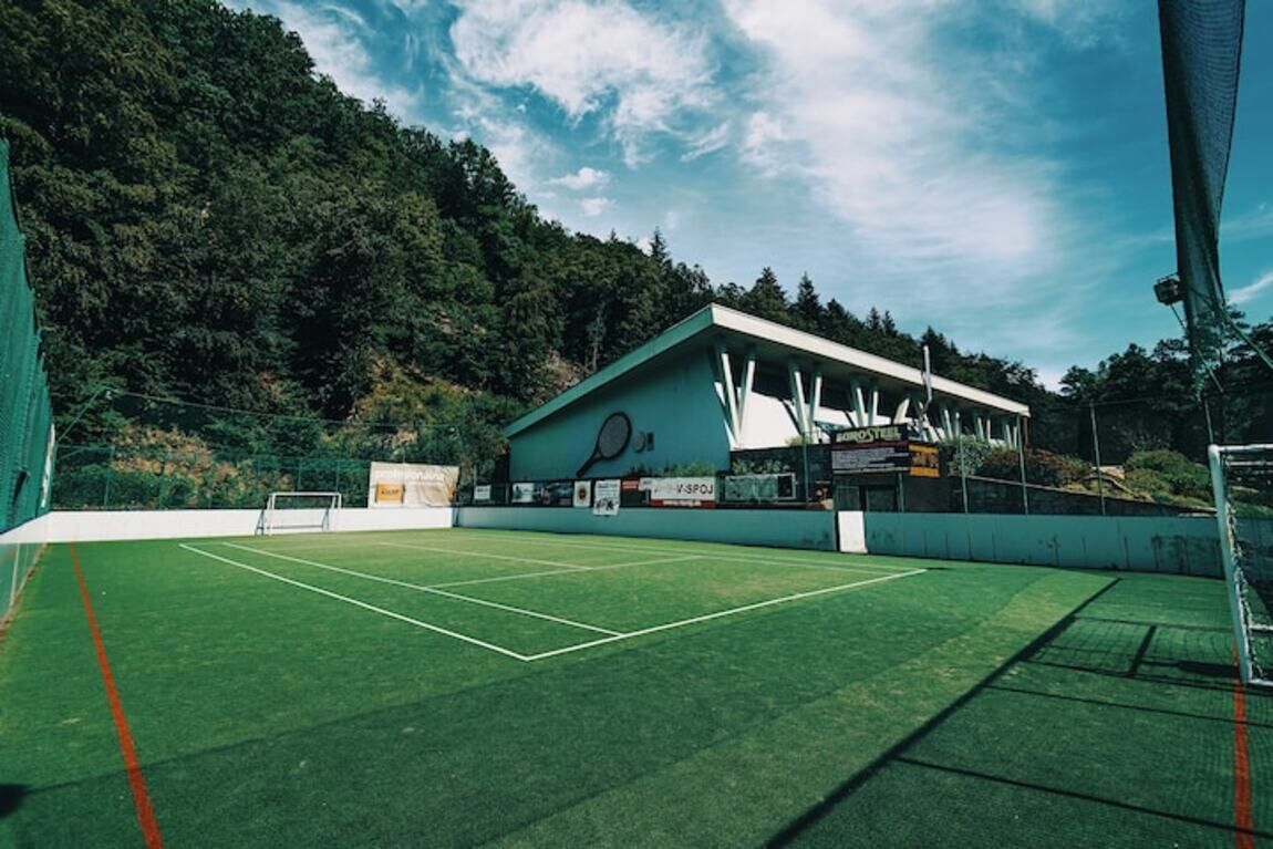 A tennis court with a building in the background, surrounded by trees.