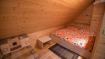 A small, cozy room with a wooden sloped ceiling, a bed with a patterned bedspread, a small bedside table, and a rug on the floor.
