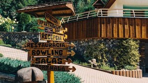A wooden signpost with multiple directional arrows pointing to various amenities such as apartments, a restaurant, bowling, and a sauna.