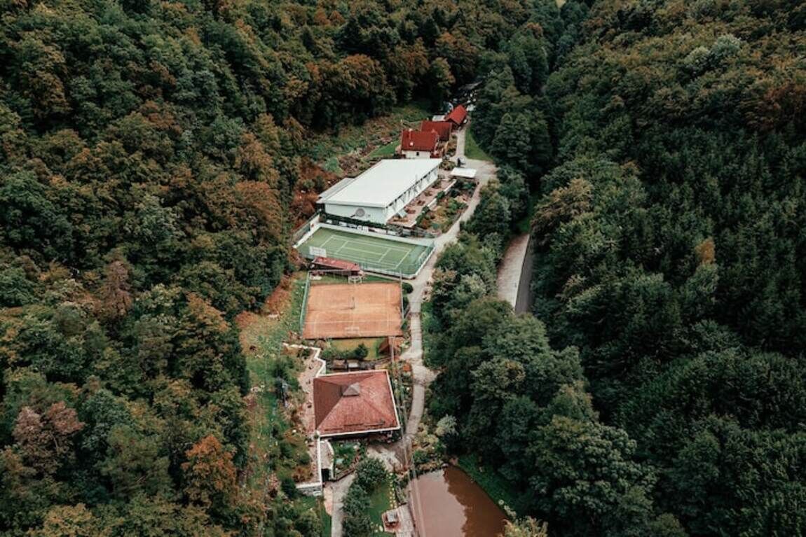 An aerial view of a property with multiple buildings, a tennis court, and a river.