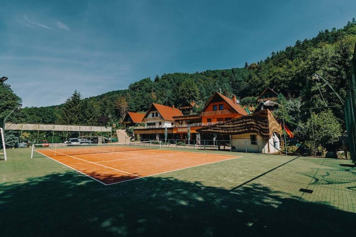 En tennisbane med net, omgivet af en bygning med flere vinduer og et tag.