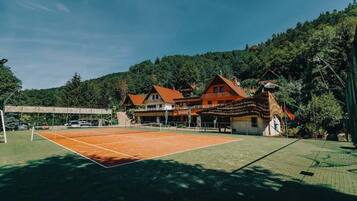 En tennisbane med net, omgivet af en bygning med flere vinduer og et tag.