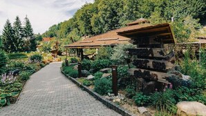 A rustic wooden building with a sloped roof, surrounded by lush greenery and a paved pathway leading to it.