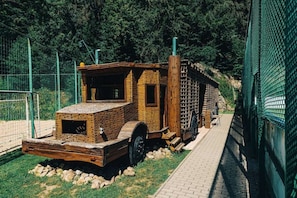 A brick structure with a chimney, a wheel, and a ladder, surrounded by a green fence and trees. - Charming chalet for 8 people, 3BD, 2BT, kitchen (Zvolen)