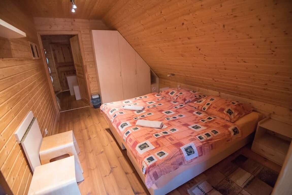 A small, wooden room with a bed, a chair, and a wardrobe.