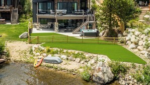Een modern, twee verdiepingen tellend landhuis met een terras met uitzicht op een rivier, omringd door weelderige begroeiing en een rotsachtig landschap.