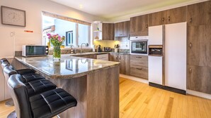 A modern kitchen with a central island, bar stools, wooden cabinets, stainless steel appliances, and a large window providing natural light. - Port Tara Holiday Home, close to Portballintrae Harbour and the Giant's Causeway (Portballintrae, Bushmills)