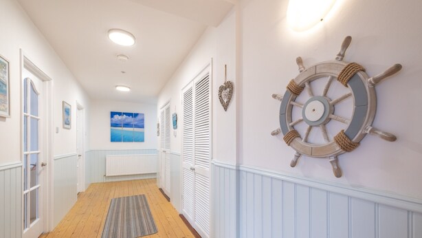 A hallway with wooden flooring, white walls, and a ship's wheel decoration. - Port Tara Holiday Home, close to Portballintrae Harbour and the Giant's Causeway (Portballintrae, Bushmills)