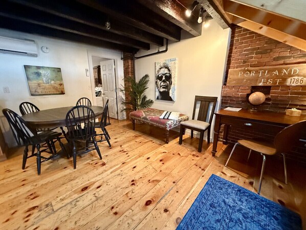 Un comedor con piso de madera, una mesa con sillas, un banco y un letrero en la pared.
