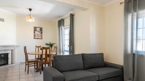 A living room with a gray sofa, wooden dining table, chairs, and a fireplace. - Peniche Terrace - Spacious apartment in the center (Peniche)