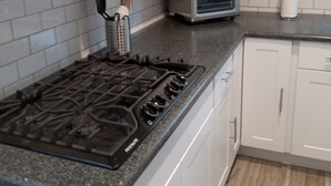 Ett kök med en gasspis, en liten ugn med grillfunktion och vita skåp.