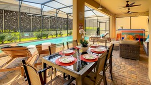 Un área de comedor al aire libre con luz solar, un recinto de vidrio, una piscina y una zona de bar.