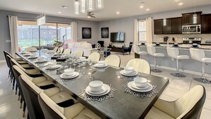 Una cocina moderna con armarios oscuros, una isla grande y un comedor con una mesa larga dispuesta para seis comensales.
