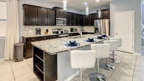 Una cocina moderna con armarios oscuros, electrodomésticos de acero inoxidable, encimera de granito y taburetes de bar blancos.