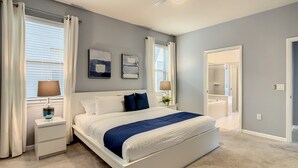 Un dormitorio con cama, mesitas de noche, ventilador de techo y baño visible a través de una puerta abierta.