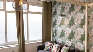A room with a large bed, a window with curtains, a hanging light fixture, and a wall with a leaf pattern. - Canopée - Lovely studio with A/C Rhône riverbank (Lyon)