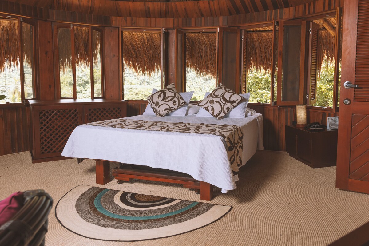 Dormitorio con estructura de madera, una cama, un tapiz tejido y vistas al exterior.