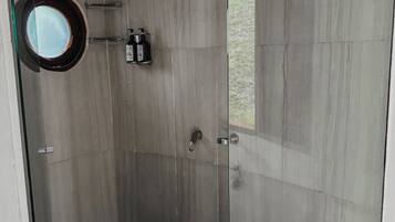 Una ducha moderna con puerta de cristal, un espejo circular y un cabezal de ducha de mano.