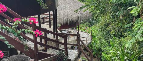 A wooden staircase leading to a thatched-roof structure with a view of lush greenery and a body of water.