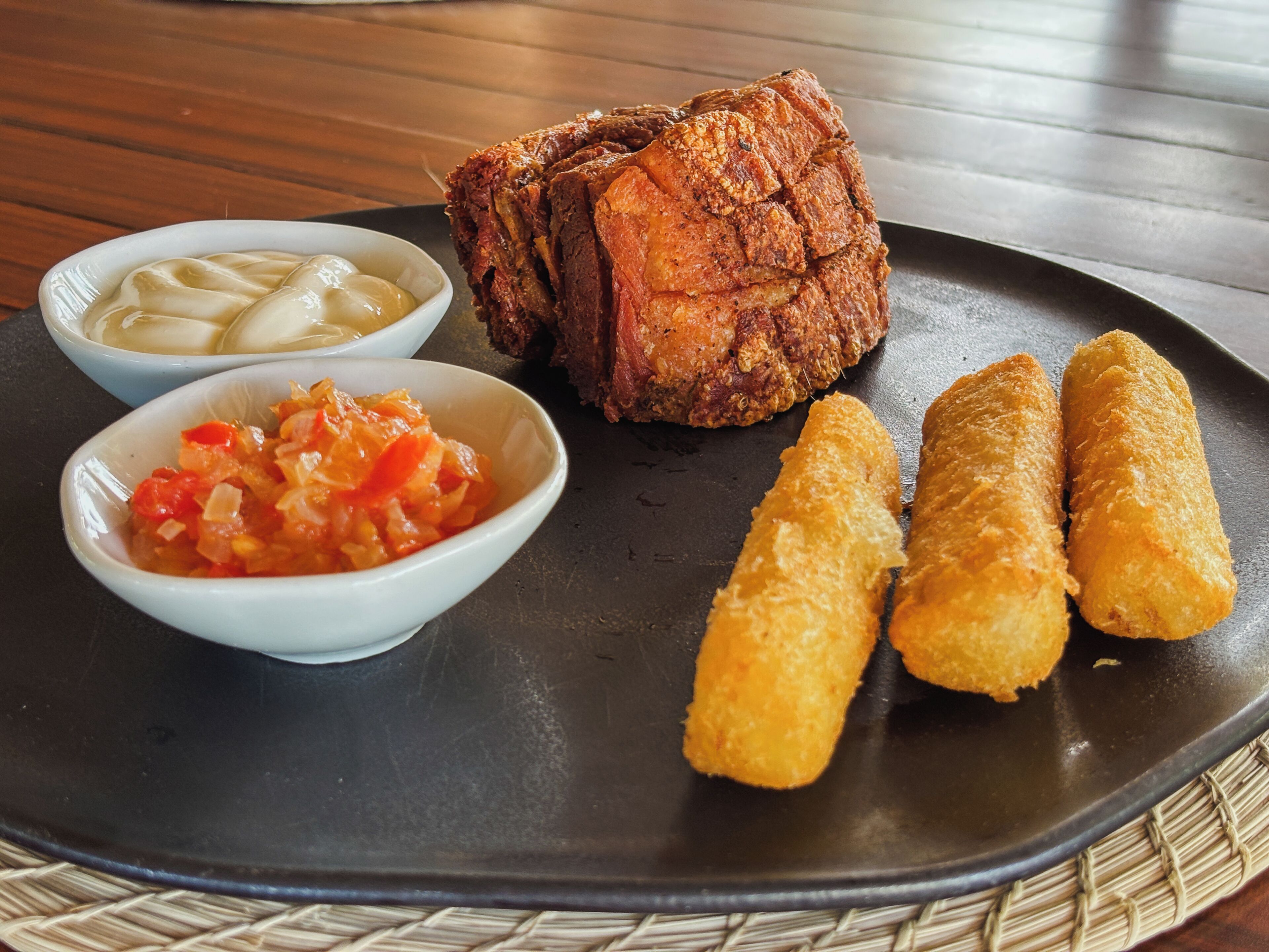 A plate with fried meat, two small bowls of dips, and three fried snacks.