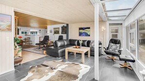 Un salon moderne avec un canapé en cuir, une table basse et un tapis en peau de vache. On y trouve également un coin repas avec des chaises et une table, ainsi qu’une cuisine en arrière-plan.