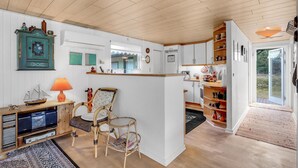 Une cuisine compacte avec des meubles blancs, un plafond en bois et un petit coin repas agrémenté de chaises en osier.