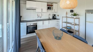 Une cuisine moderne avec des armoires blanches, un four encastré, une machine à café et un luminaire suspendu.