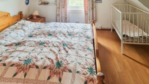 Ein Schlafzimmer mit einem hölzernen Bett, einem Babybett, einem Fenster mit Vorhängen und einem Regal mit Dekoration.