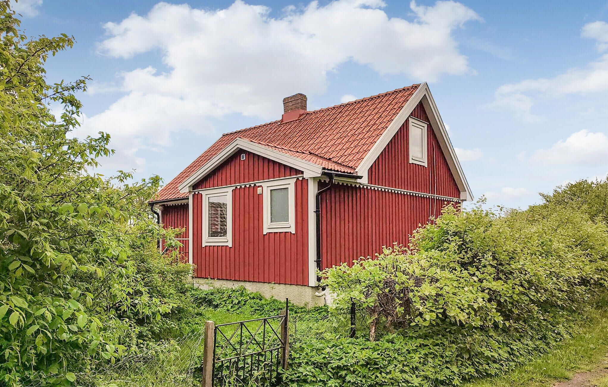 Ett rött trähus med ett brant tak, omgivet av frodig grönska.