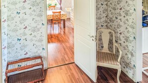 Ein Zimmer mit blumigem Wandpapier, Holzboden, einer weißen Tür und einem Stuhl.