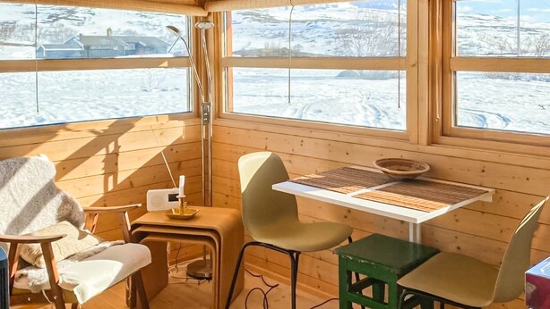 Ein gemütliches Blockhaus mit Holzwänden und großen Fenstern, einem Tisch mit Stühlen und einem kleinen Heizgerät.