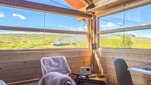 Ein gemütliches Cabin-Zimmer mit großem Fenster und Blick auf eine grüne Landschaft sowie ein Haus in der Ferne.