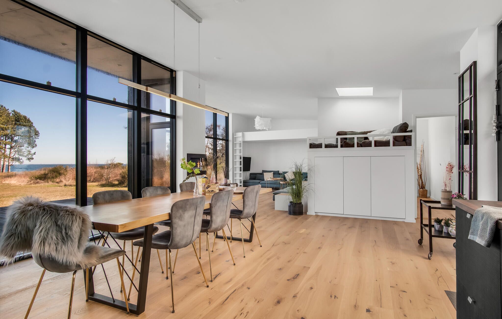 A modern interior with a dining area, kitchen, and large windows overlooking a natural landscape.