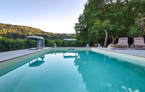 En rektangulær swimmingpool med klart vand, omgivet af en terrasse med liggestole og en pavillon.