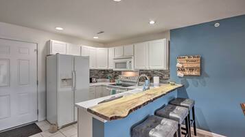 A kitchen with white cabinets, a wooden island with bar stools, a microwave, and a wall-mounted sign.