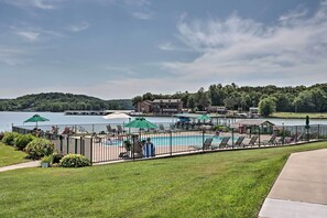 A pool area with lounge chairs and umbrellas, surrounded by a fence, with a lake and buildings in the background.