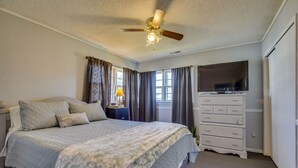 Une chambre à coucher comprenant un lit, une commode, un téléviseur et un ventilateur de plafond.
