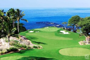 A golf course with a view of the ocean, palm trees, and a clear sky.