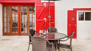 Un espace extérieur aménagé avec des chaises en osier et une table en verre, une porte rouge et une fenêtre donnant sur un paysage agréable.