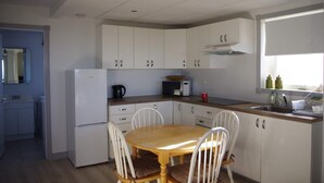 Une cuisine de taille réduite avec des meubles blancs, une table à manger en bois et un micro-ondes encastré.