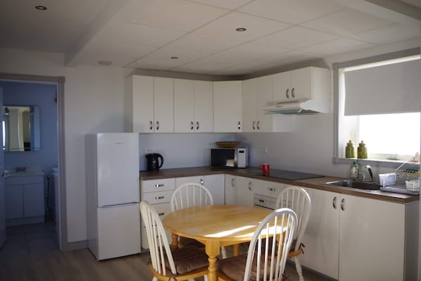 Una cocina compacta con armarios blancos, una mesa de comedor de madera y un microondas integrado.