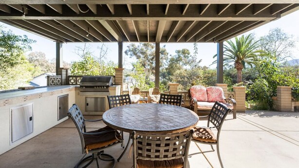 Eine Terrassenausstattung im Freien mit rundem Tisch, Stühlen, einem Grill und einer gepolsterten Sitzgruppe.