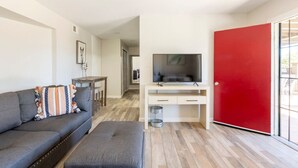 Ein modernes Wohnzimmer mit einem grauen Sofa, einem Fernseher auf einem weißen Schrank und einer roten Tür.
