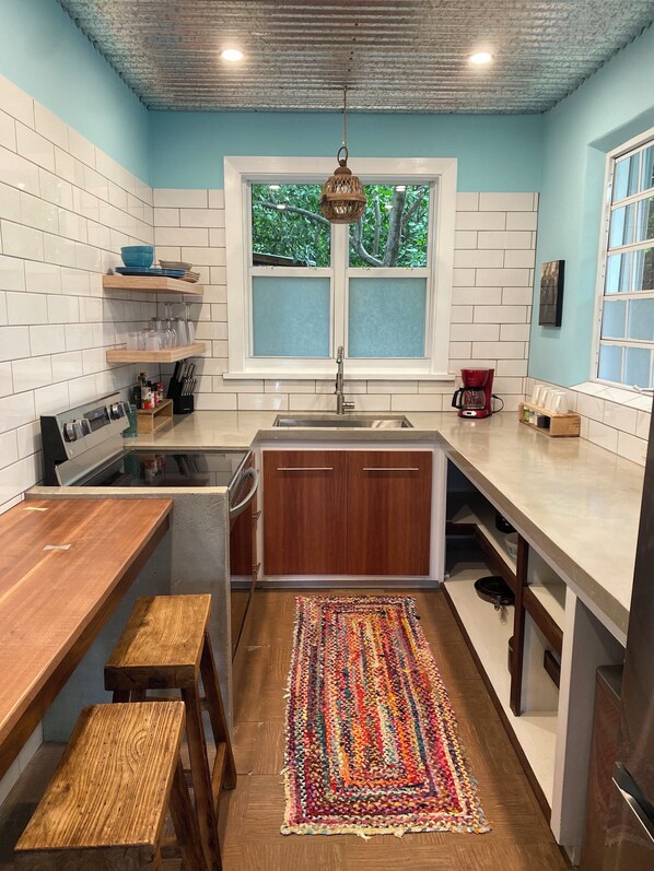 Una cocina compacta con paredes blancas y azules, encimera de madera, un lavamanos y una ventana con vidrio esmerilado.