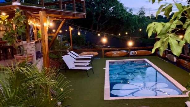 Un espace piscine doté d’une structure en verre, entouré de chaises longues et illuminé de guirlandes lumineuses.